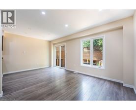 A spacious room with wooden flooring and a large window with blinds.