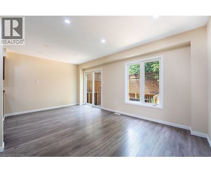 A spacious room with wooden flooring and a large window with blinds.