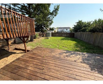 A wooden deck leads to a backyard with a fence and green grass.