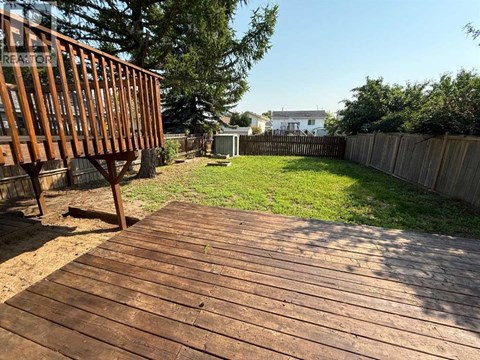 A wooden deck leads to a backyard with a fence and green grass.