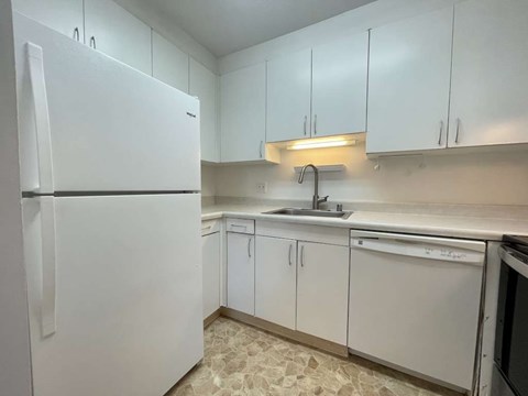 A white refrigerator is in a kitchen with white cabinets.