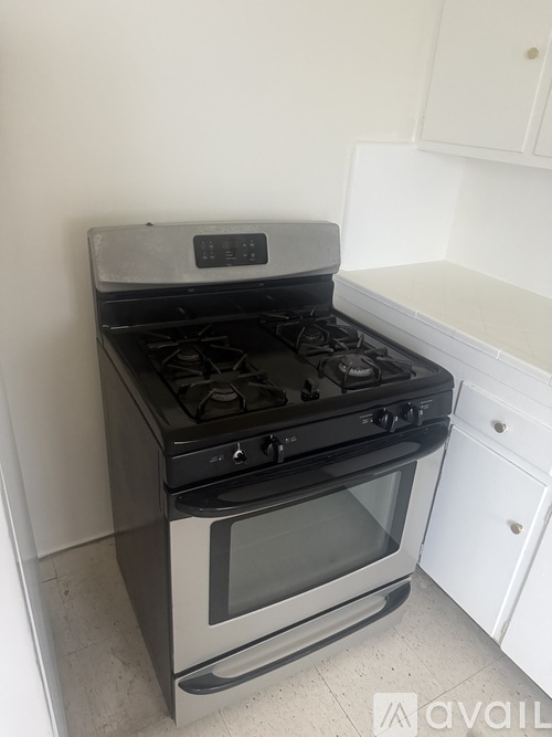 A black and silver stove top oven with a glass door is in a kitchen with white cabinets.