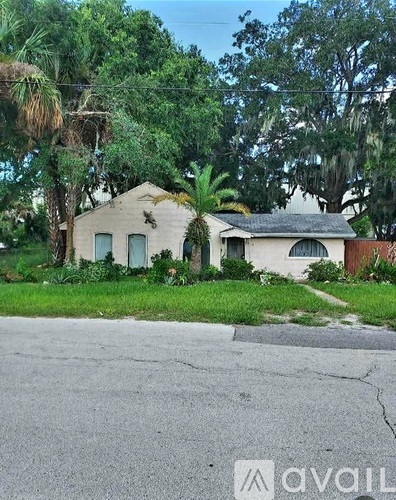 A house with a faded white exterior is surrounded by greenery.