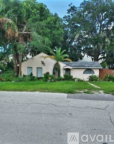 A house with a faded white exterior is surrounded by greenery.