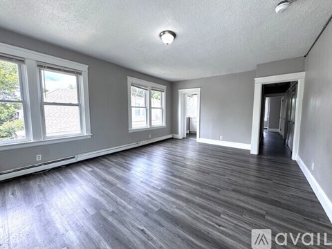 A spacious room with wooden flooring and large windows.