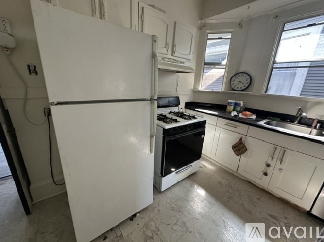 A white refrigerator stands in a kitchen with a black stove and white cabinets.