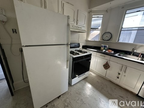 A white refrigerator stands in a kitchen with a black stove and white cabinets.