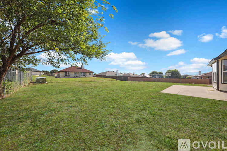 A grassy backyard with a tree and a house in the background.