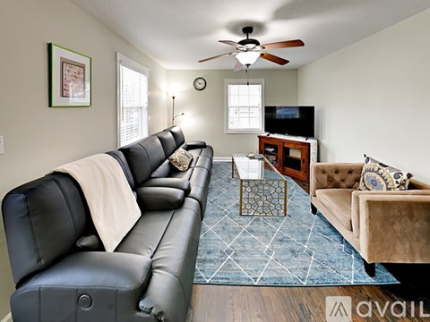 A living room with a black leather couch and a blue rug.