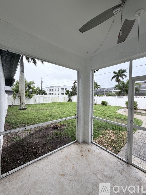 A patio with a fan and a view of a yard and a building.