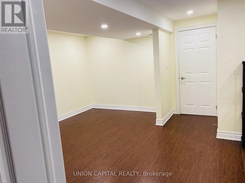 A room with wooden flooring and white walls, with a door on the right side.