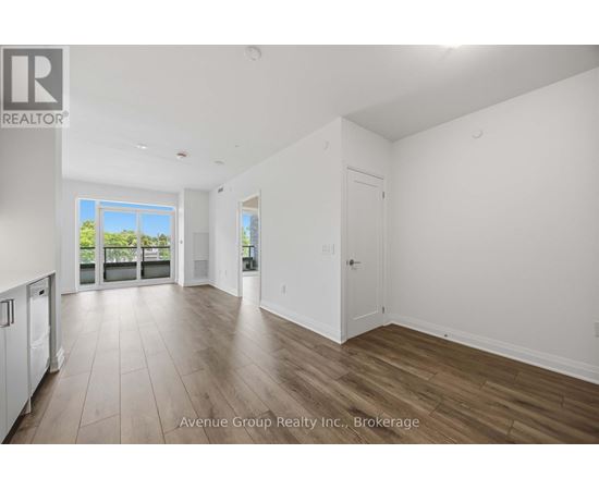 A spacious room with wooden flooring and a large window overlooking a balcony.