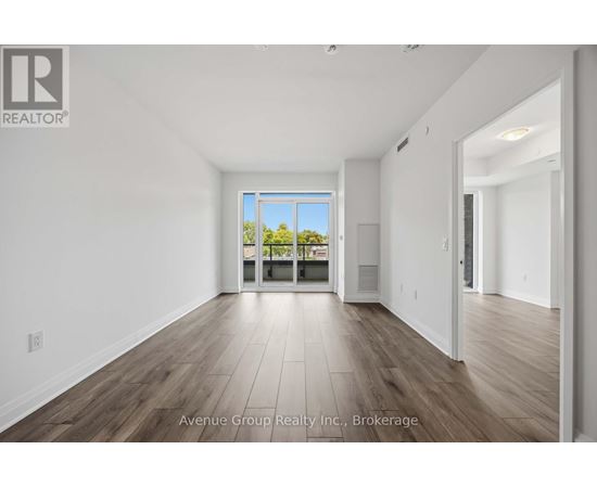 A large, empty room with wooden floors and a view of trees through a glass door.