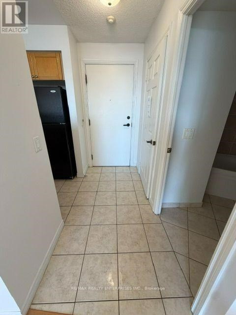 A hallway with a black fridge and white walls.