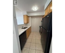 A kitchen with a black refrigerator, white countertops, and wooden cabinets.