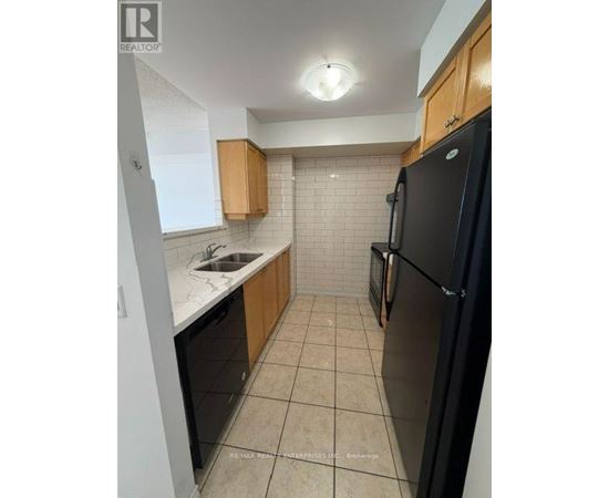A kitchen with a black refrigerator, white countertops, and wooden cabinets.