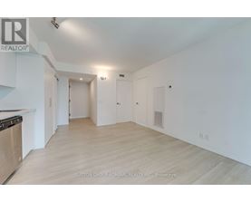 A spacious room with light wood flooring and white walls, with a stove on the left side.