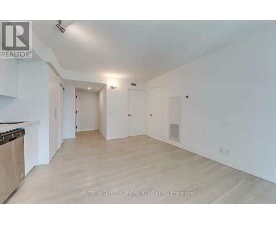 A spacious room with light wood flooring and white walls, with a stove on the left side.