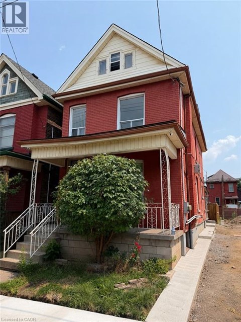 A red house with a white window and a tree in front.