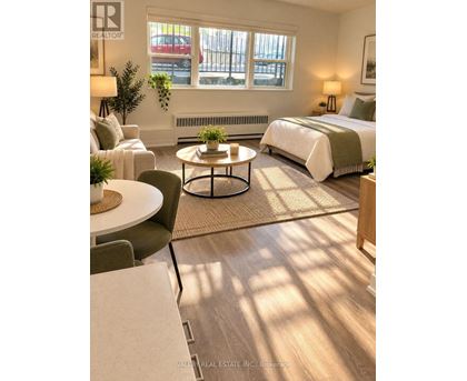 A bedroom with a bed, a couch, a chair, a table, and a window with a view of a parking lot.