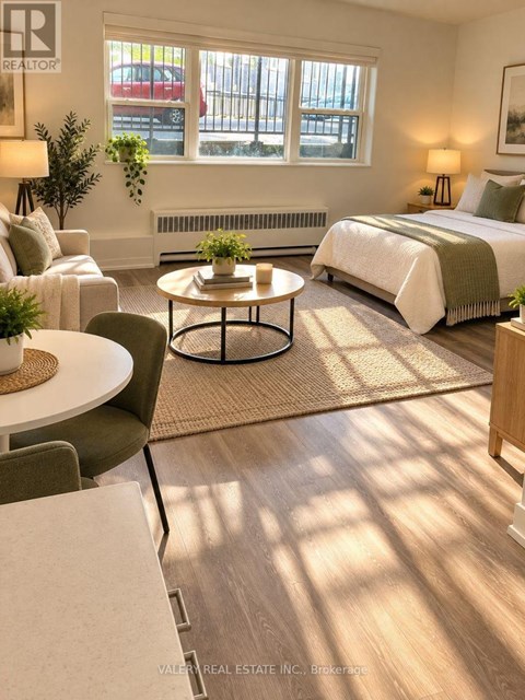 A bedroom with a bed, a couch, a chair, a table, and a window with a view of a parking lot.