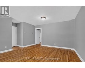 A room with wooden floors and white walls, with a doorway leading to another room.