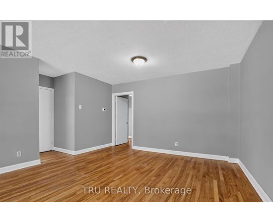 A room with wooden floors and white walls, with a doorway leading to another room.