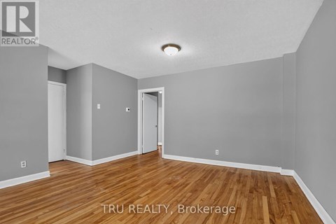 A room with wooden floors and white walls, with a doorway leading to another room.