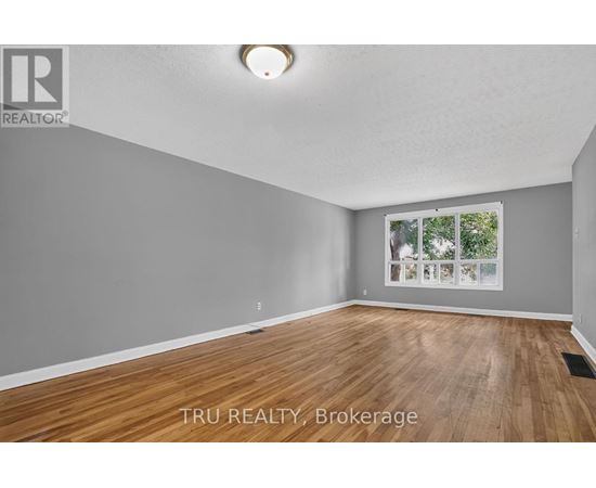 A room with wooden flooring and a window showing trees outside.