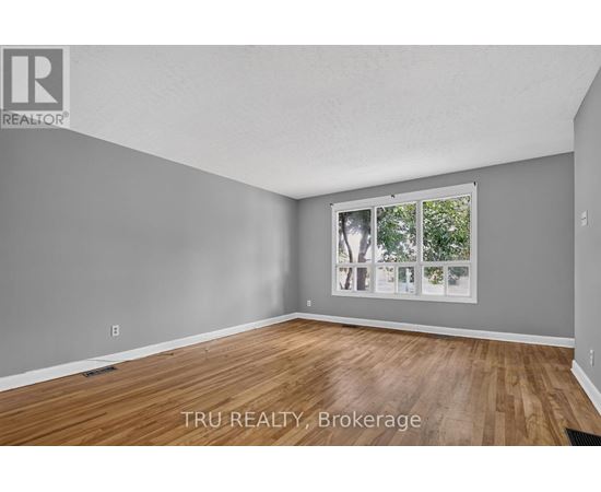 A room with wooden flooring and a window showing trees outside.