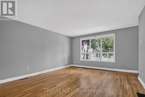A room with wooden flooring and a window showing trees outside.
