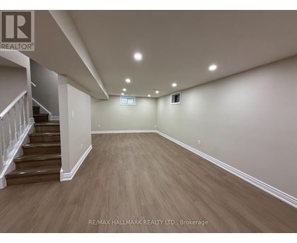 A spacious room with wooden flooring and a staircase on the left side.