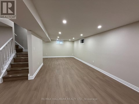 A spacious room with wooden flooring and a staircase on the left side.