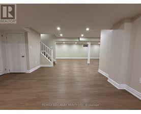 A spacious room with wooden flooring and white walls, with a staircase on the left side.