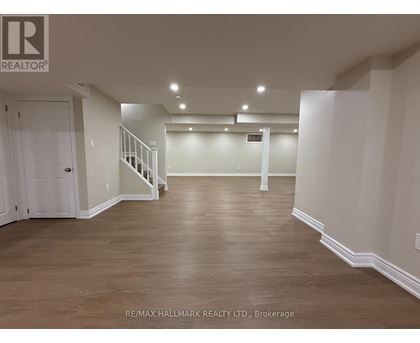 A spacious room with wooden flooring and white walls, with a staircase on the left side.