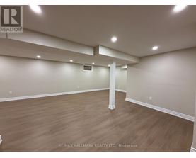 A spacious room with wooden flooring and white walls, with a column in the middle.