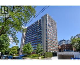 A tall building with many windows is surrounded by trees and parked cars.