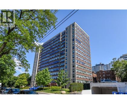 A tall building with many windows is surrounded by trees and parked cars.
