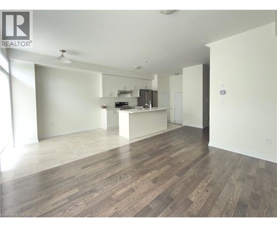 A spacious room with wooden flooring and a kitchen area in the background.