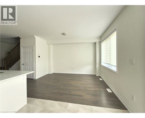 A spacious room with wooden flooring and a staircase on the left side.
