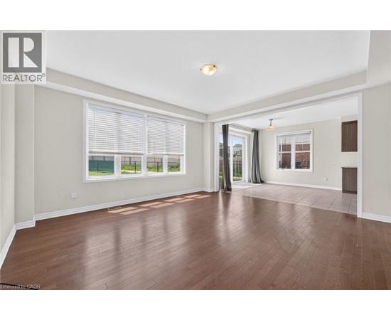 A spacious room with wooden flooring and a large window with blinds.
