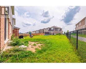 A grassy area in front of a row of houses with a fence on the right side.