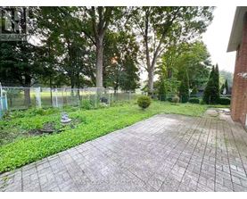 A backyard with a paved walkway, a fence, and trees.