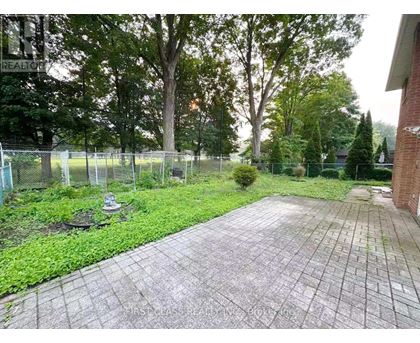 A backyard with a paved walkway, a fence, and trees.