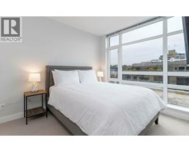 A bedroom with a bed, nightstand, lamp, and a flat screen TV mounted on the wall.