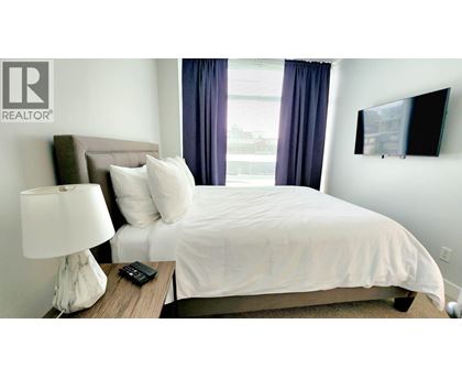 A bedroom with a bed, nightstand, lamp, and a flat screen TV mounted on the wall.