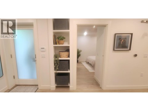 A bedroom with a bed, a shelf with plants, and a picture on the wall.