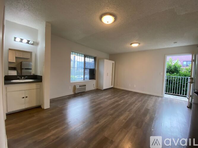 A spacious living room with wooden floors and a kitchen area to the left.