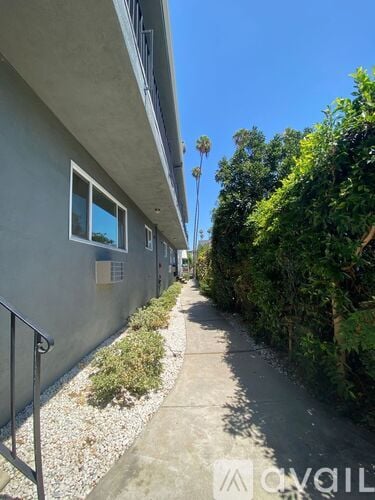 A concrete pathway leads through a residential area with a building on the left and a tree on the right.