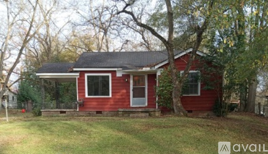 A red house with a white door and windows is surrounded by trees.